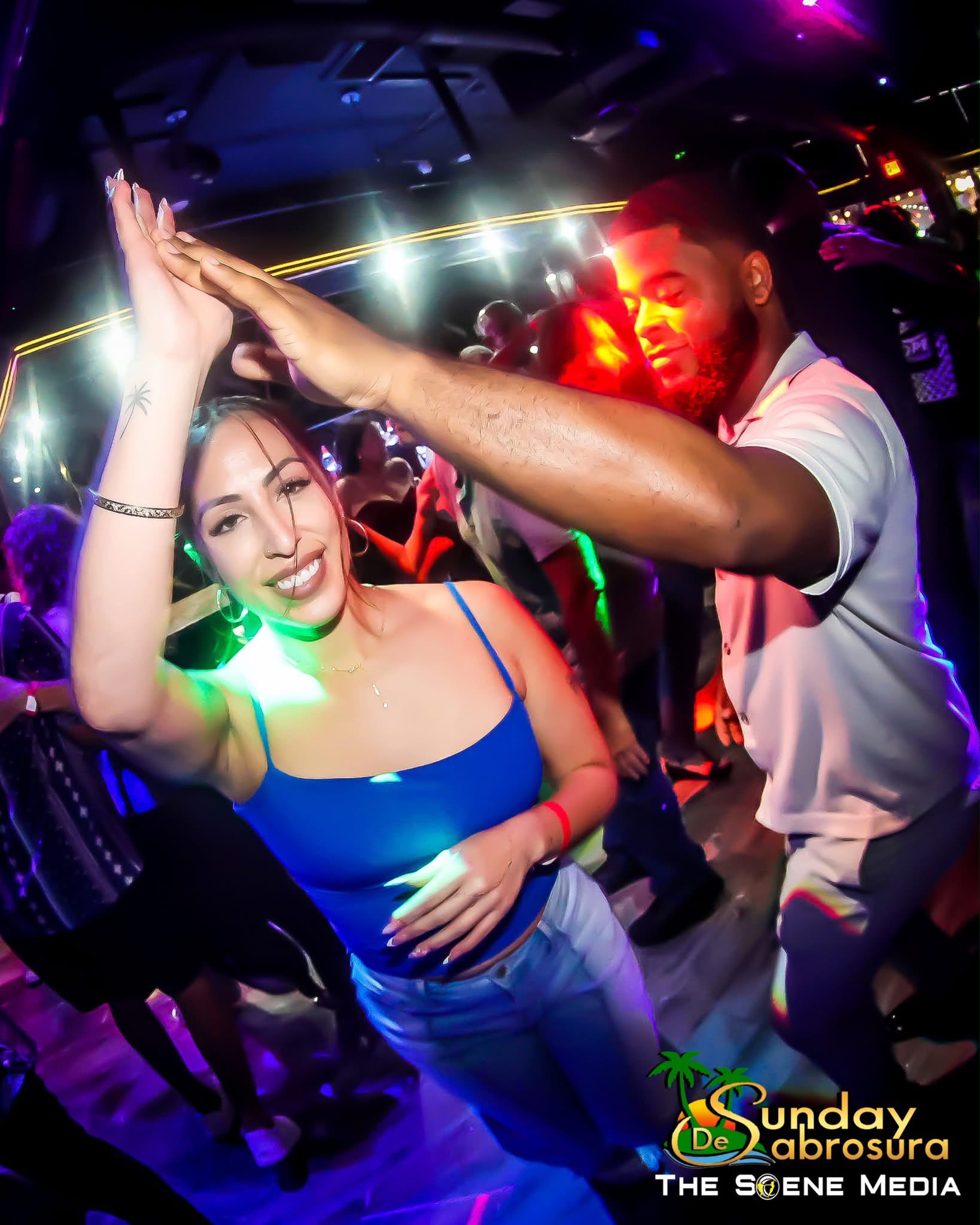 Partners dancing under colorful lights at Sunday de Sabrosura
